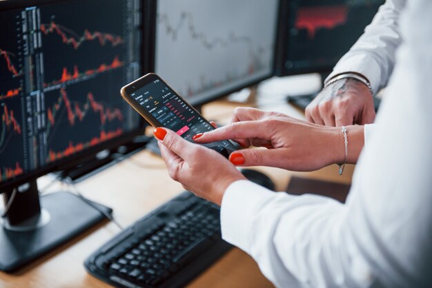 Vista ravvicinata delle mani delle persone con telefono e grafici su di esso. Gli agenti di cambio hanno un lavoro.