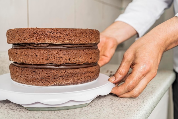 Vista ravvicinata delle mani di un pasticcere che mette una torta al cioccolato su un vassoio bianco in una cucina.