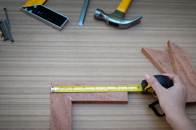 Vista ravvicinata delle mani di una donna che misurano la tavola di legno con un metro a nastro con una raccolta di utensili manuali da lavoro per il legno, set di strumenti con il fai da te (fai da te)