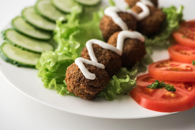 Vista ravvicinata di falafel con salsa su piatto con verdure a fette su sfondo bianco