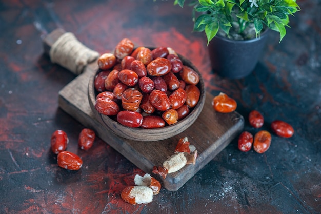 Vista ravvicinata di frutti freschi di silverberry crudi in una ciotola su un tagliere di legno e un vaso di fiori su uno sfondo di colori misti