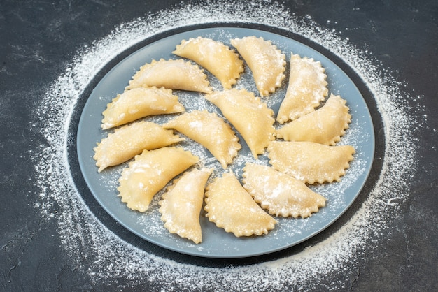 Vista ravvicinata di gnocchi crudi fatti in casa su un piatto blu con farina intorno su superficie nera