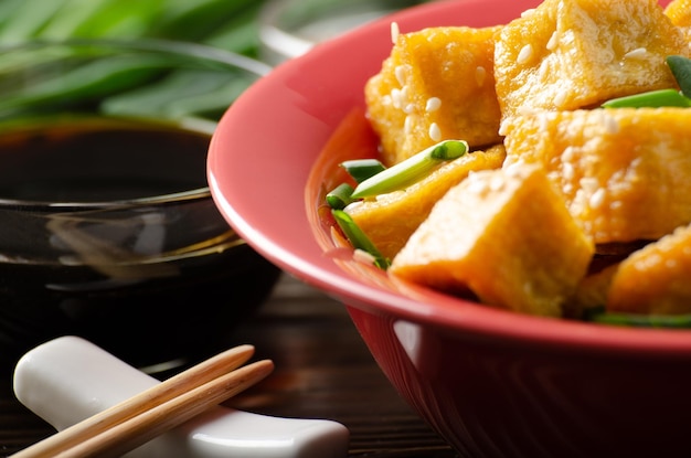 Vista ravvicinata di pezzi di tofu fritti croccanti con erba cipollina e sesamo in un piatto di argilla