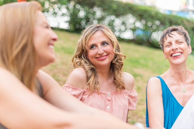Vista ravvicinata di tre donne adulte sedute nel parco ridendo. Belle donne mature che si divertono insieme nel parco.