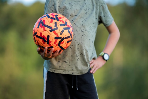 Vista ravvicinata di un adolescente che tiene una palla da calcio arancione Scatto del suo busto