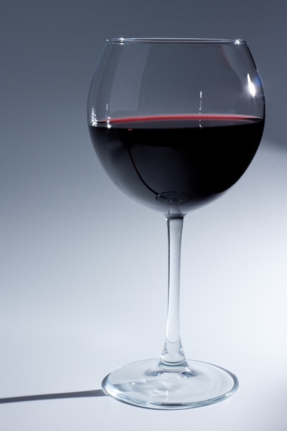 Vista ravvicinata di un bicchiere di vino con vino rosso su uno sfondo grigio graduato