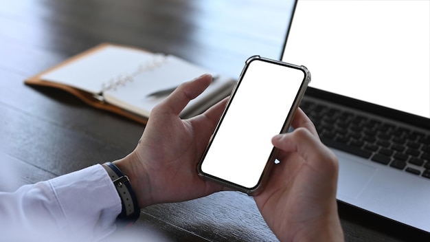 Vista ravvicinata di un impiegato maschio seduto davanti al computer portatile e utilizzando il telefono cellulare