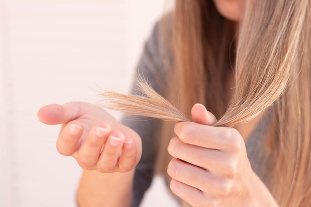 Vista ravvicinata di una donna irriconoscibile che tiene i capelli danneggiati con doppie punte con messa a fuoco selettiva e sfondo sfocato