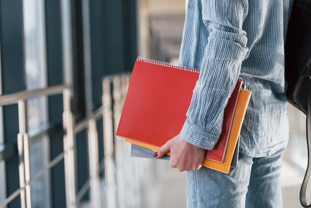 Vista ravvicinata di una giovane studentessa che si trova nel corridoio di un college e tiene dei blocchetti per appunti