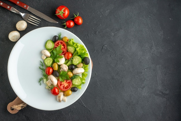 Vista ravvicinata di verdure fresche tritate di olive nere e gialle su un piatto bianco e posate su sfondo nero con spazio libero