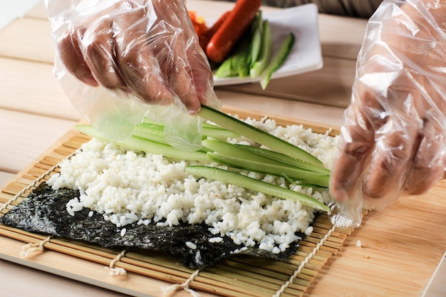 Vista ravvicinata Processo di preparazione di Rolling Sushi/Gimbap/Kimbap. Nori e Riso Bianco. Riso del rotolo di tocco delle mani dello chef. Lo chef aggiunge Kyuri (cetriolo) all'interno di Kimbap Rice Rol