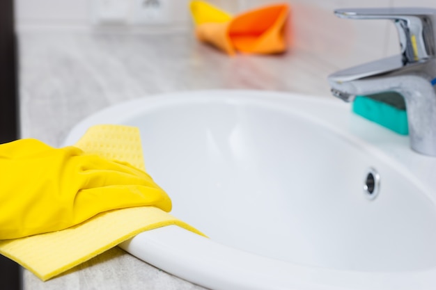 Vista ravvicinata sul bordo di pulizia delle mani con guanti di gomma gialla del lavandino in avorio con rubinetto cromato e spugna nelle vicinanze