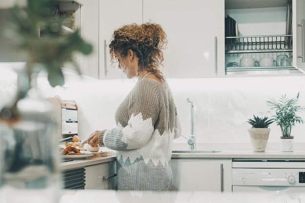 Vista reale laterale della donna che cucina a casa nella cucina moderna minimale bianca