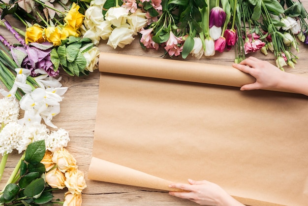 Vista ritagliata del fiorista con carta artigianale e fiori colorati su superficie di legno