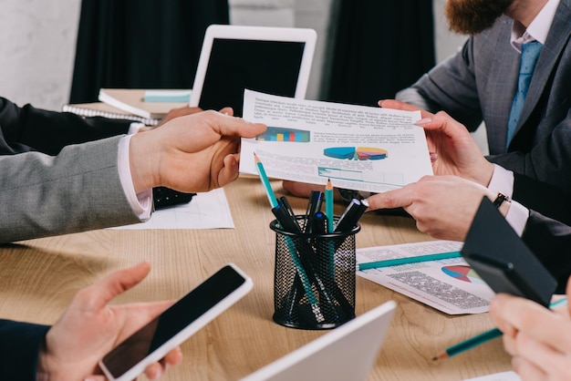 Vista ritagliata dell'uomo d'affari che dà il diagramma al partner mentre i colleghi di lavoro lavorano al tavolo in