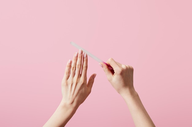 Vista ritagliata della donna che lima le unghie con lima per unghie isolata su rosa