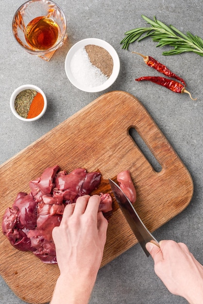 Vista ritagliata della donna che taglia carne cruda sul tagliere tra spezie bicchiere di cognac peperoni e