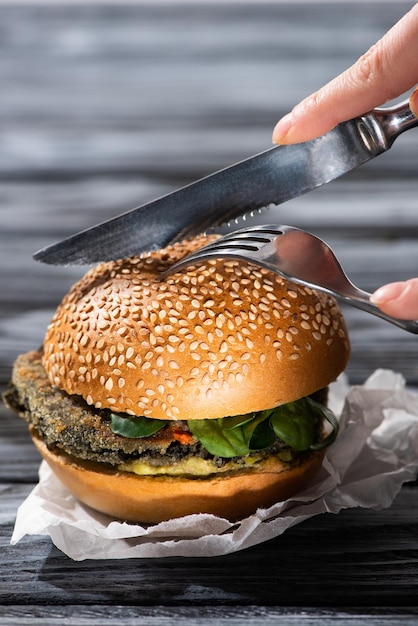 Vista ritagliata della donna che taglia gustoso hamburger vegano con forchetta e coltello