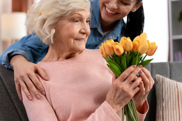 Vista ritagliata della giovane donna che porta fiori alla madre anziana a casa Relazioni tra madre e figlia e celebrazione del concetto di festa della mamma felice