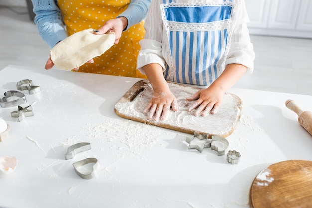 Vista ritagliata della madre che tiene la pasta e la figlia che aggiunge farina in cucina