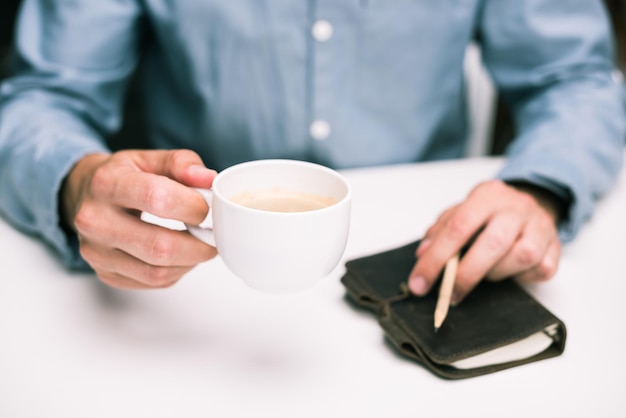 Vista ritagliata delle mani maschili con tazza di caffè e diario