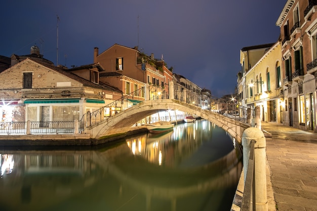 vista serale di architettura antica illuminata, barche galleggianti e riflessi di luce nell'acqua dei canali