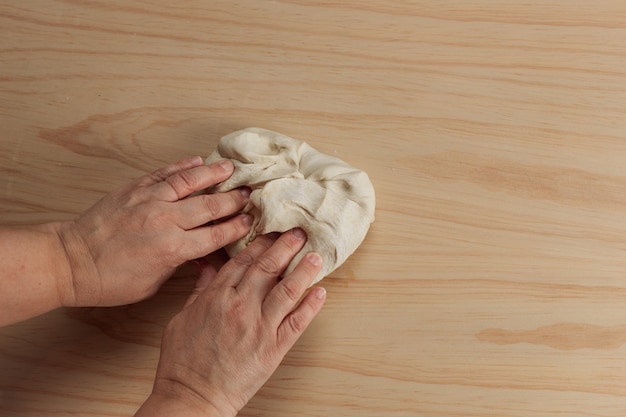 Vista sopraelevata delle mani di una donna adulta che impasta la pasta della pizza in una tavola di legno nella cucina