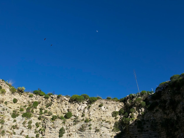 vista su una roccia di pietra con il verde contro un cielo blu in una giornata di sole a San Giovanni Gemini