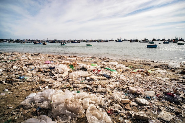 Vista su una spiaggia sabbiosa vicino al villaggio di pescatori con molta spazzatura. Inquinamento di una costa. Mui Ne