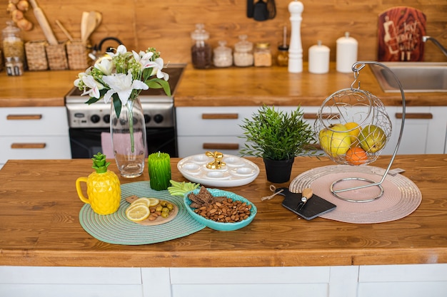 Vista sul bancone della cucina moderna in legno con vari cibi e snack. Vaso di gigli e piatto di uova con coniglietto dorato in cima. Concetto di Pasqua.