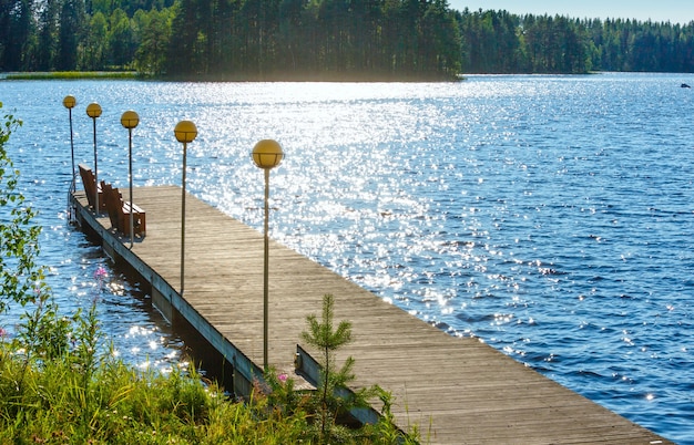 Vista sul lago estivo con foresta sul bordo e panchine sul molo in legno (Finlandia).