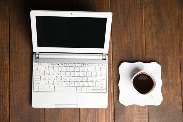 Vista sul laptop con una tazza di caffè nero sul piattino.Sfondo in legno.Da sopra
