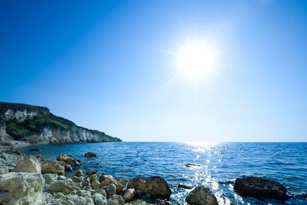 Vista sul mare di acque di mare ancora blu, spiaggia di pietra e roccia verde