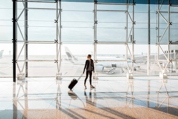 Vista sulla finestra dell'aeroporto con una donna che cammina con la valigia nella sala partenze dell'aeroporto. Vista grandangolare con spazio di copia