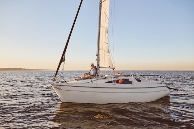 Vista sullo stile di vita di lusso della barca a vela o dello yacht che galleggia in mare con un uomo anziano rilassato che legge a