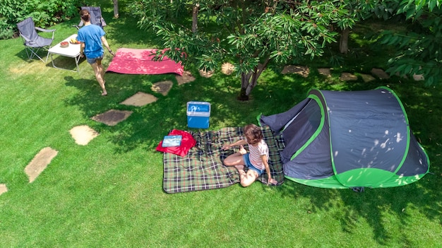 Vista superiore aerea del campeggio da sopra, madre e figlia divertendosi, tenda e attrezzatura di campeggio sotto l'albero, vacanza di famiglia nel concetto del campo all'aperto