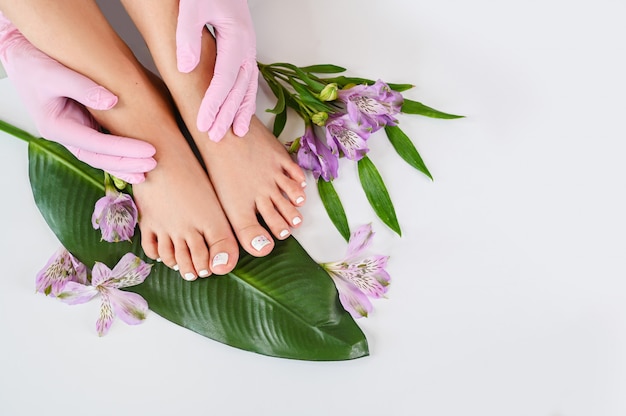 Vista superiore dei piedi femminili delle gambe della bella pelle perfetta con i fiori tropicali e la foglia di palma verde