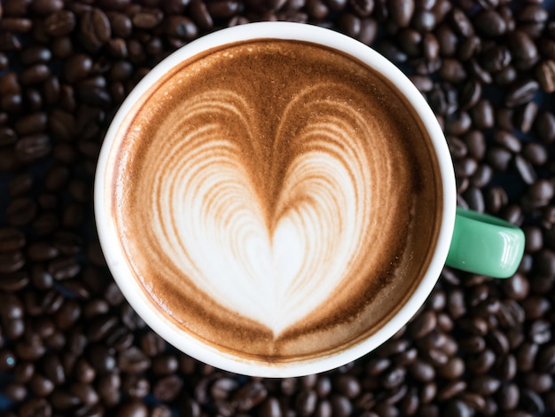 Vista superiore del caffè caldo in una tazza con bella arte del latte sul fondo dei chicchi di caffè.