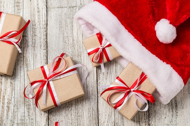 Vista superiore del cappello di Santa con i contenitori di regalo di natale su fondo di legno bianco