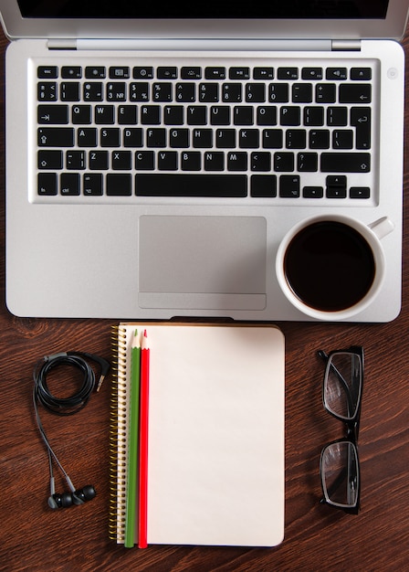 Vista superiore del computer portatile e del blocco note con i vetri e le cuffie sul desktop e sulla tazza di caffè di legno rustici.