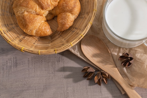 Vista superiore del croissant nel cestino, una tazza di latte, cucchiaio di legno