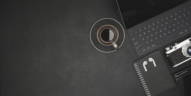 Vista superiore del posto di lavoro moderno scuro con tablet, tazza di caffè e articoli per ufficio sulla scrivania nera