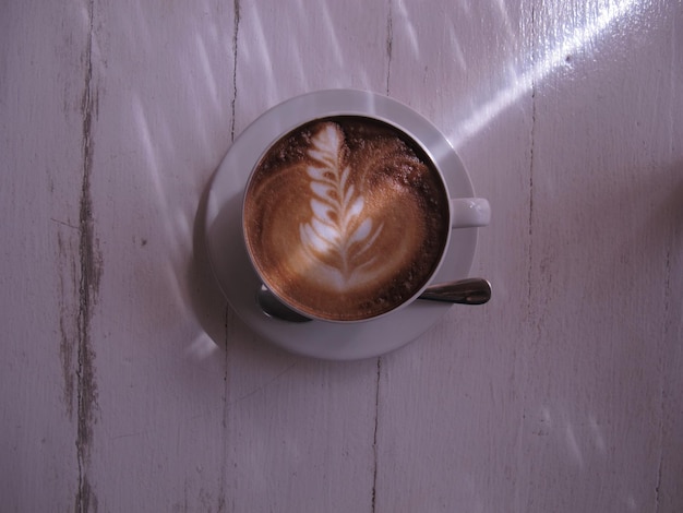 Vista superiore dell'arte del latte caldo del caffè sulla tavola di legno bianca.