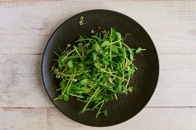 Vista superiore dell'insalata sana del vegano fatta dei germogli microgreen dei piselli e dei fagioli germogliati sulla parete di legno