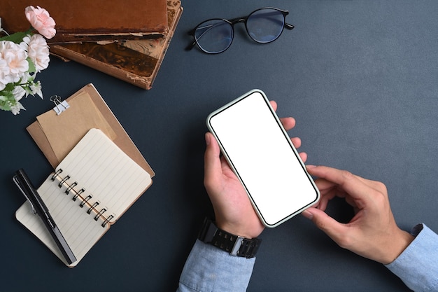 Vista superiore dell'uomo d'affari che tiene mock up smart phone con schermo vuoto sulla superficie blu scuro