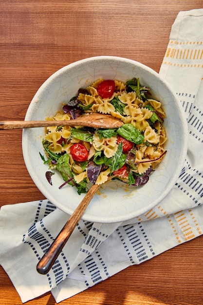 Vista superiore della ciotola con insalata di pasta e spatole vicino al tovagliolo su fondo di legno