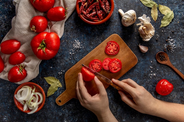 Vista superiore della persona che affetta i pomodori con il peperoncino rosso