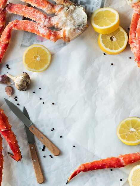 Vista superiore delle falangi di granchio fresco con limone e spezie su carta spiegazzata.