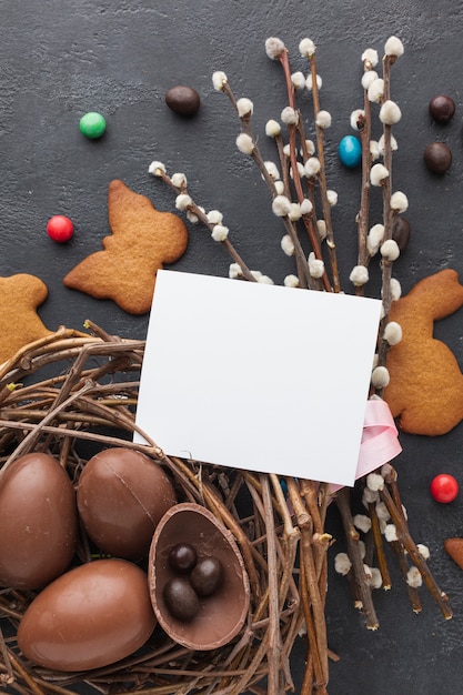 Vista superiore delle uova di Pasqua del cioccolato in nido con i biscotti e pezzo di carta sulla cima