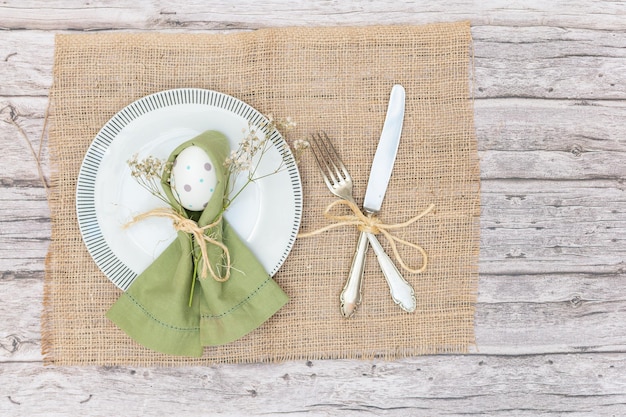 Vista superiore di un piatto con un uovo di Pasqua decorato con tovaglioli e posate